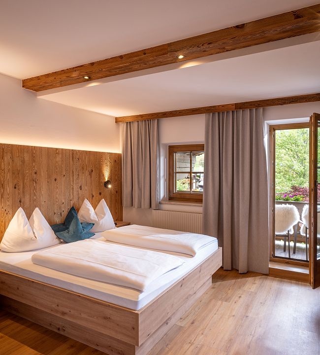 Modernes Schlafzimmer mit Altholzrückwand, Garderobe, Spiegel, TV und Balkon zum Wilden Kaiser